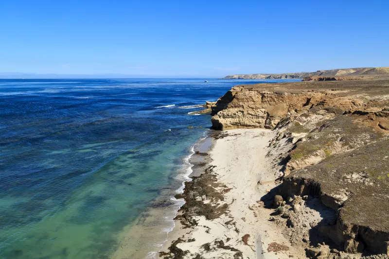 Low coastal mountains and terraces covered in dry grass leading to white sand pocket beaches and oce