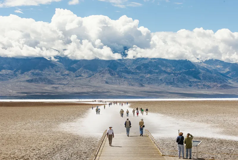 The image shows a broad, arid landscape with a wooden path leading deep into a salt flat.