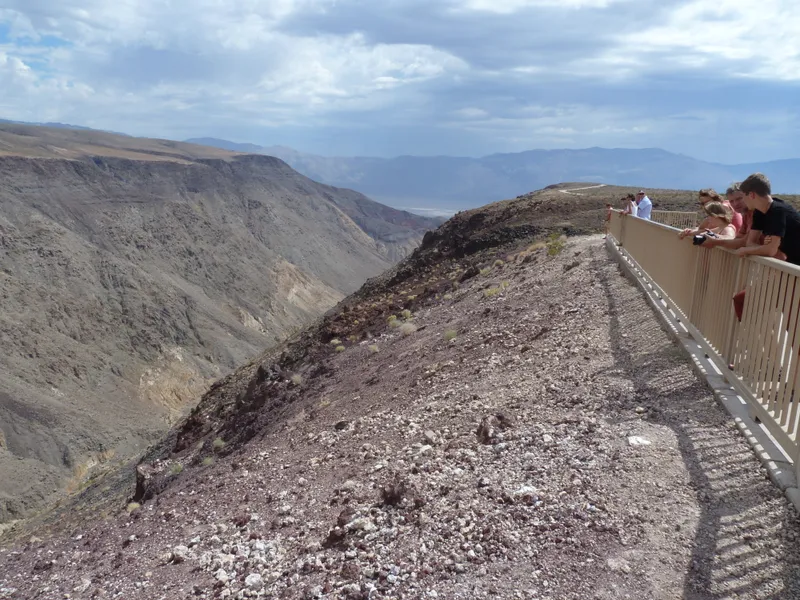 Visitors lean over a metal fence to look into a colorful deep desert canyon with dark clouds above.