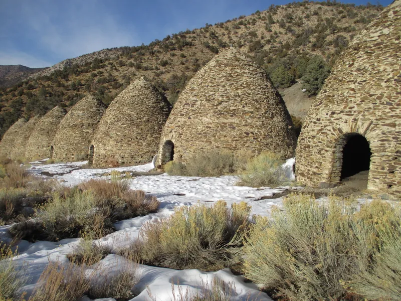 Stone and mortar beehive structures in a row in patchy snow.
