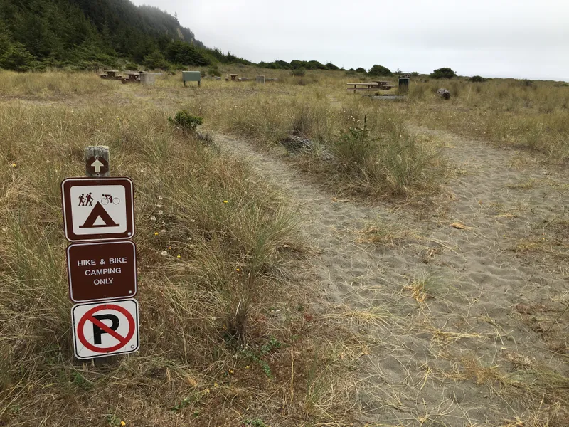 Hike and bike signs, sandy trail and a campsite on grassy dunes.